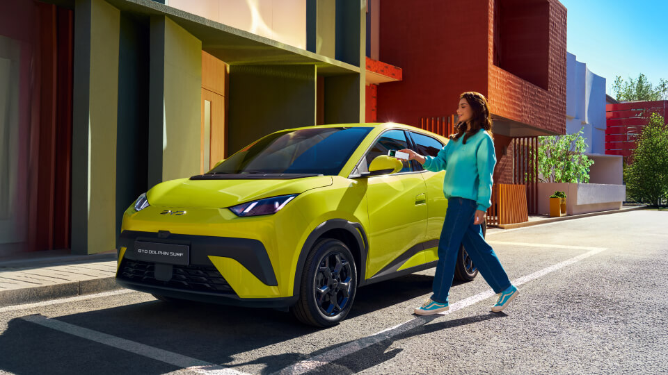 BYD Dolphin Surf in yellow, parked on suburban street with person approaching to unlock using their mobile phone