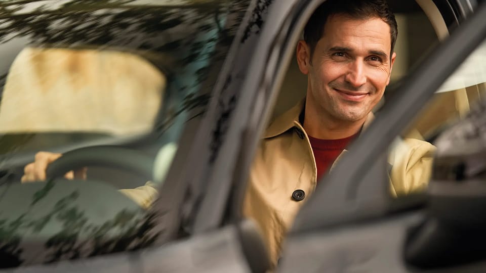 Person sitting in car with door open, smiling