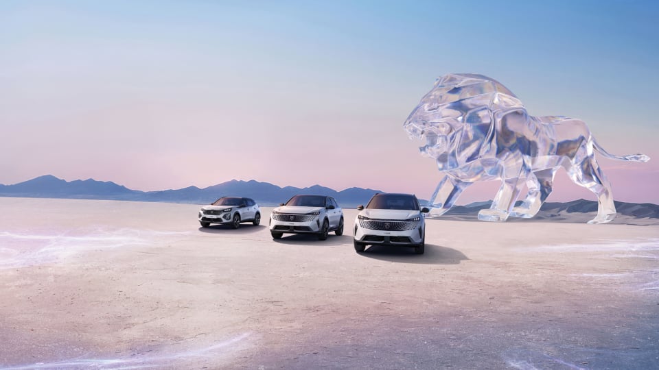 Front angled view of three Peugeot vehicles with a lion in background