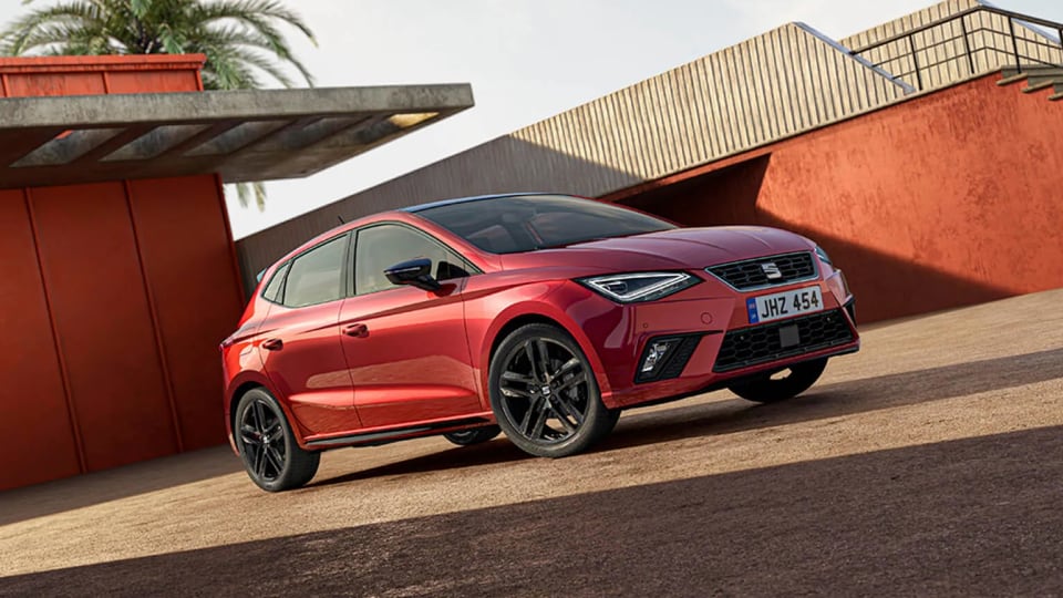 Red SEAT Ibiza FR parked on a sunlit driveway with modern architecture and palm tree in the background.