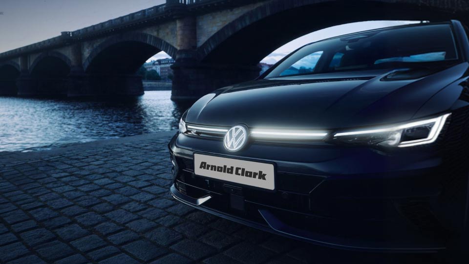 Volkswagen Golf at dusk beside a city river and bridge